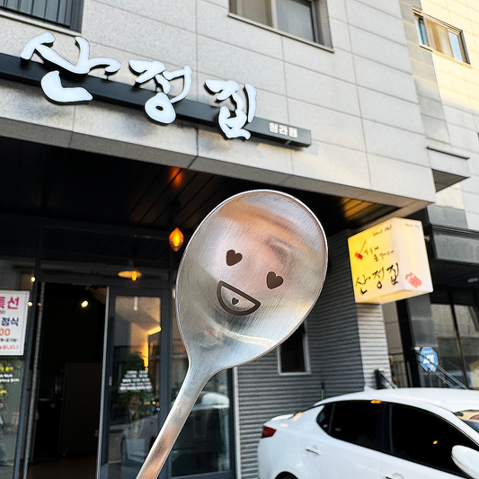 Standing in front of the restaurant sign, ready to dig in with a spoon.