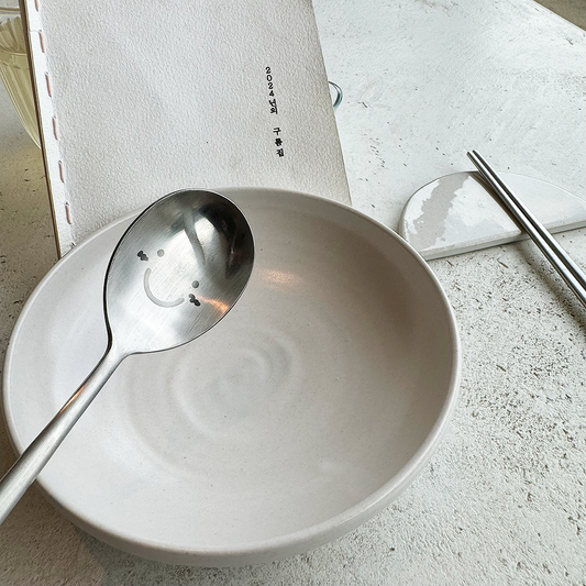 A white plate holds the menu, while a smiling spoon and chopsticks rest on the table.