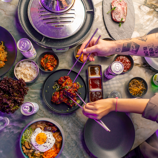 Korean-style BBQ is set on the table, with bibimbap and flat chopsticks reaching for the side dishes.