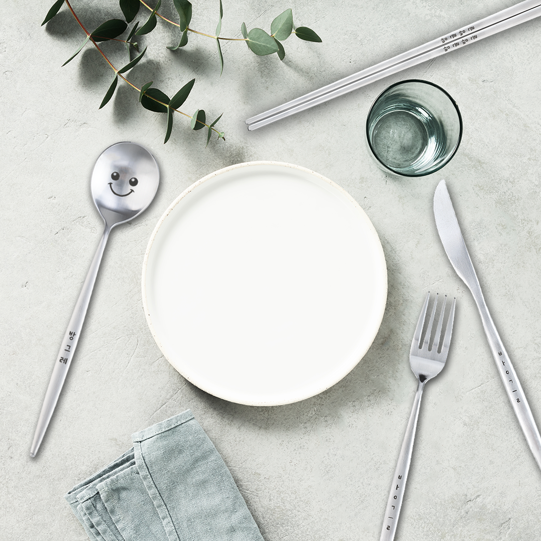 Bapmoo's spoon, fork, chopsticks, and knife together with a white plate and a green-toned table setting.