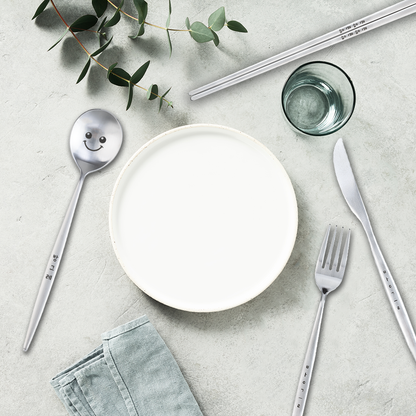 Bapmoo's spoon, fork, chopsticks, and knife together with a white plate and a green-toned table setting.